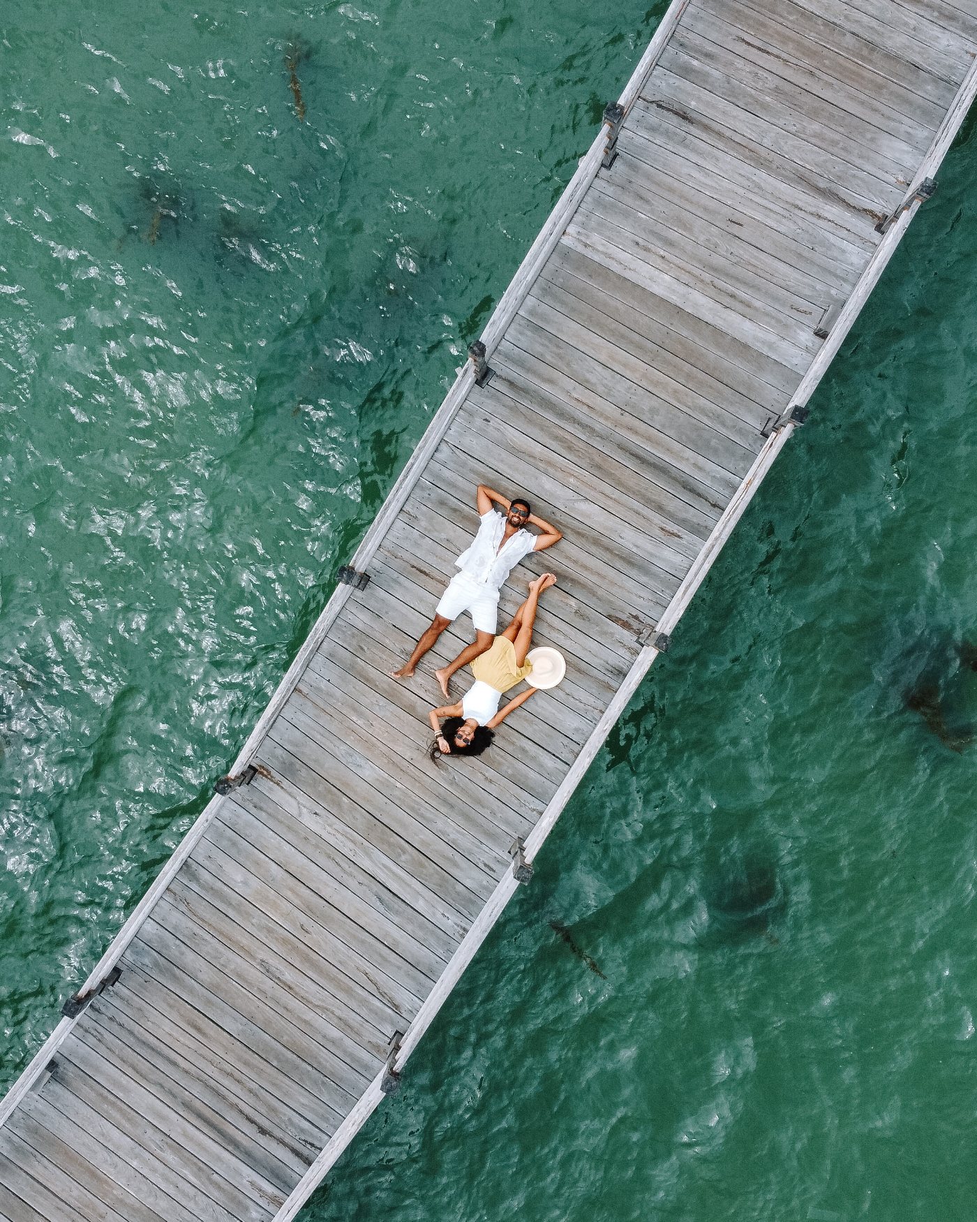 Aerial view of Prachi and Harsh lying on a wooden jetty over turquoise water